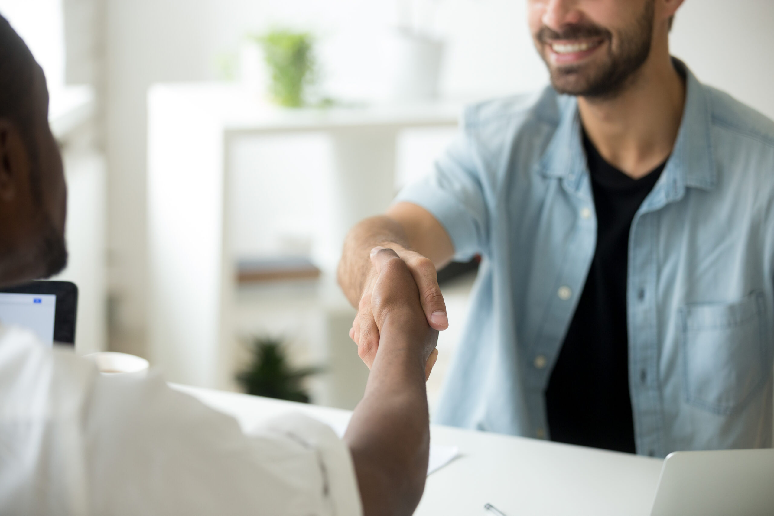 Young diverse multiracial businessmen shaking hands, african american and caucasian entrepreneurs binding contract deal with handshake establishing multi-ethnic partnership concept, close up view